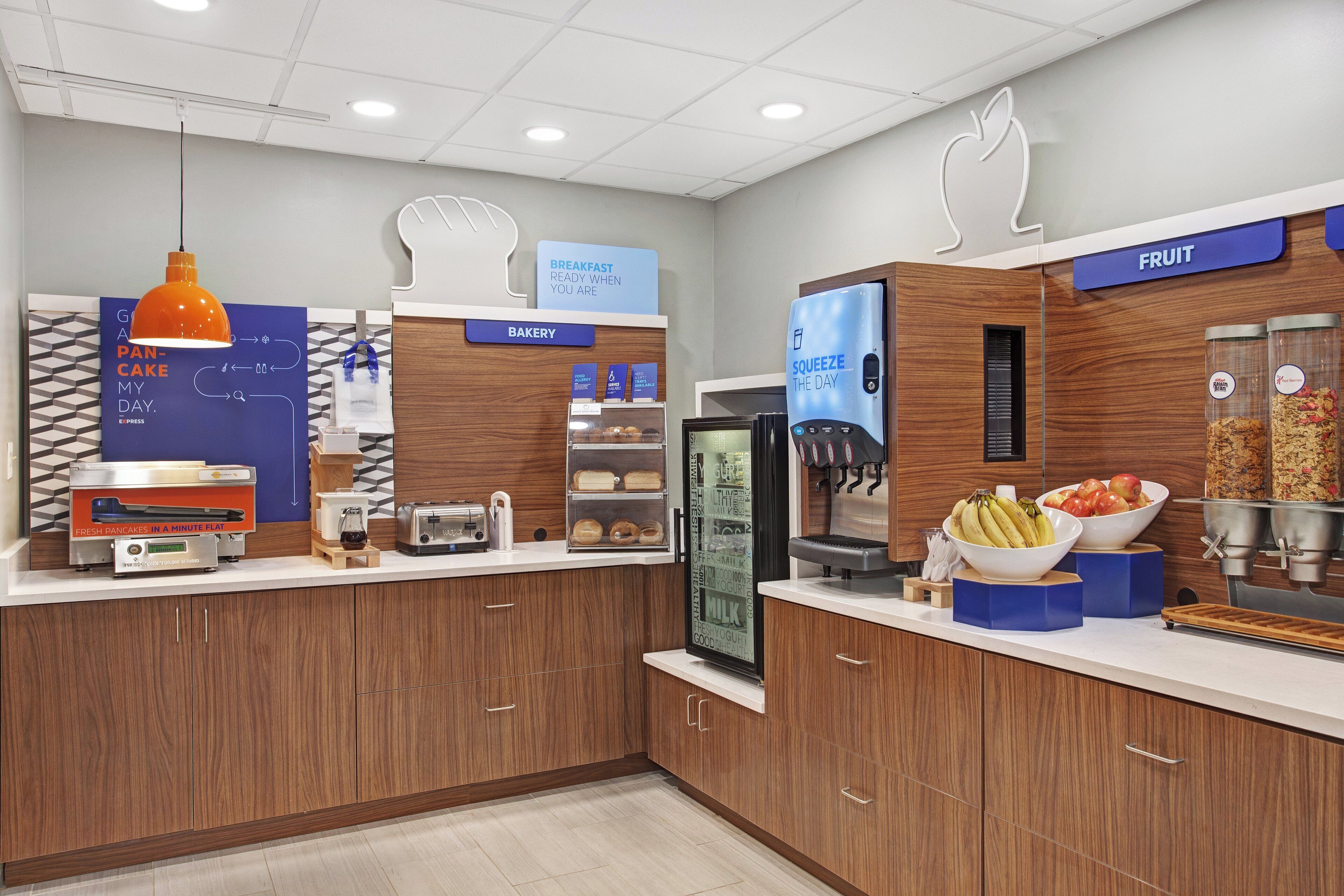 A breakfast area with a bakery section, a fruit display, and a juice dispenser.