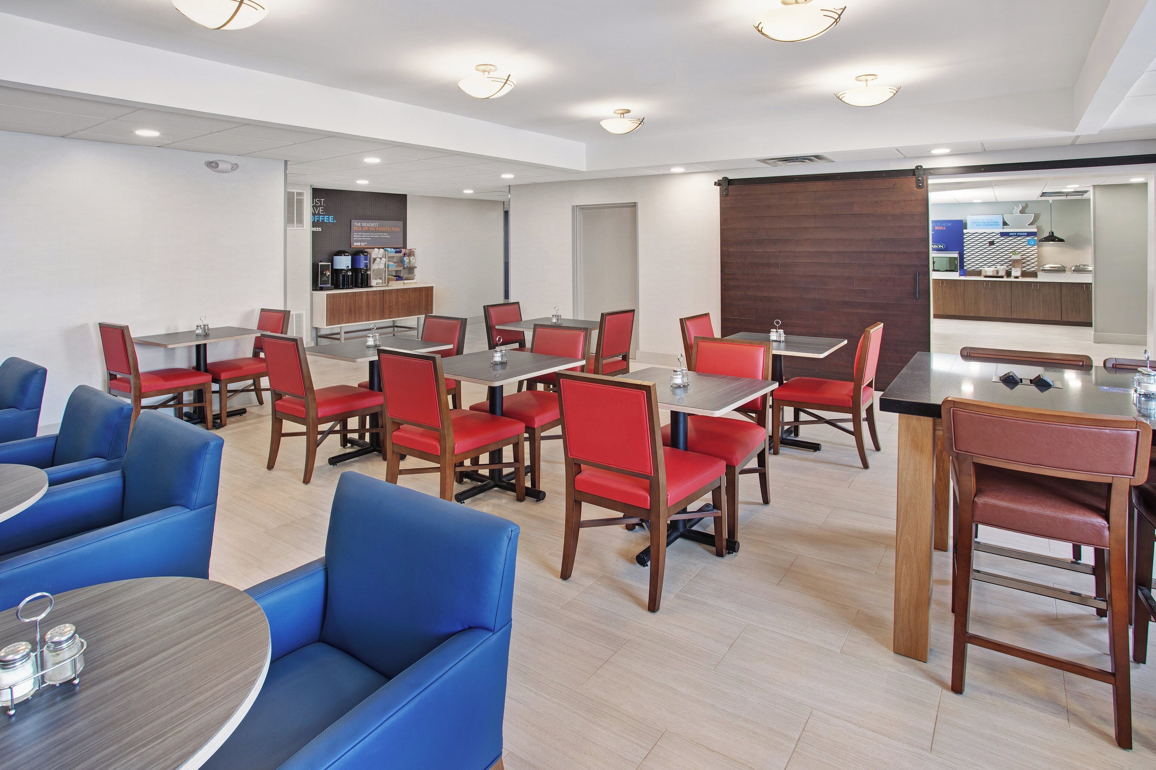 A hotel dining area with multiple tables and chairs, a coffee station, and a kitchen area.