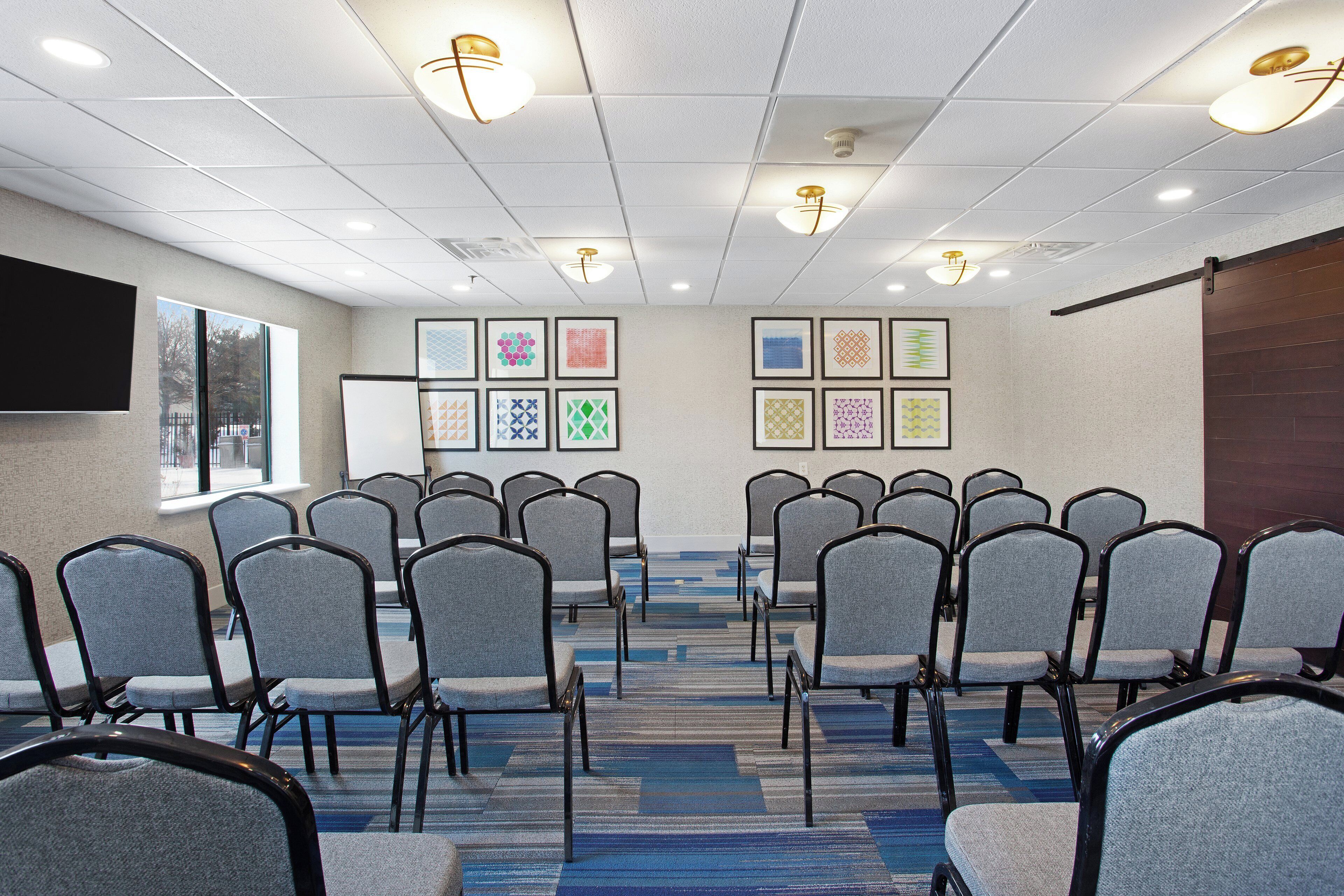 A conference room with rows of chairs, a projector screen, and framed artwork on the walls.