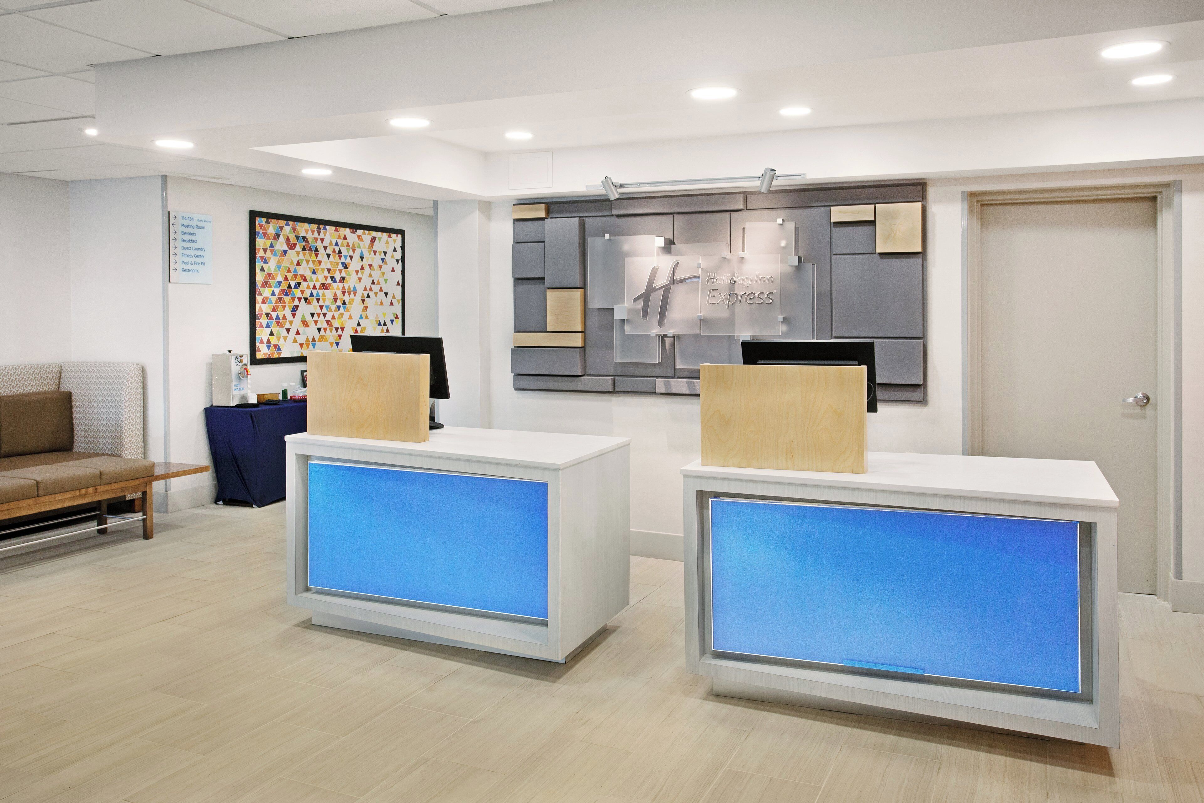 A reception area with two reception desks, a wall-mounted sign, and a colorful geometric artwork.