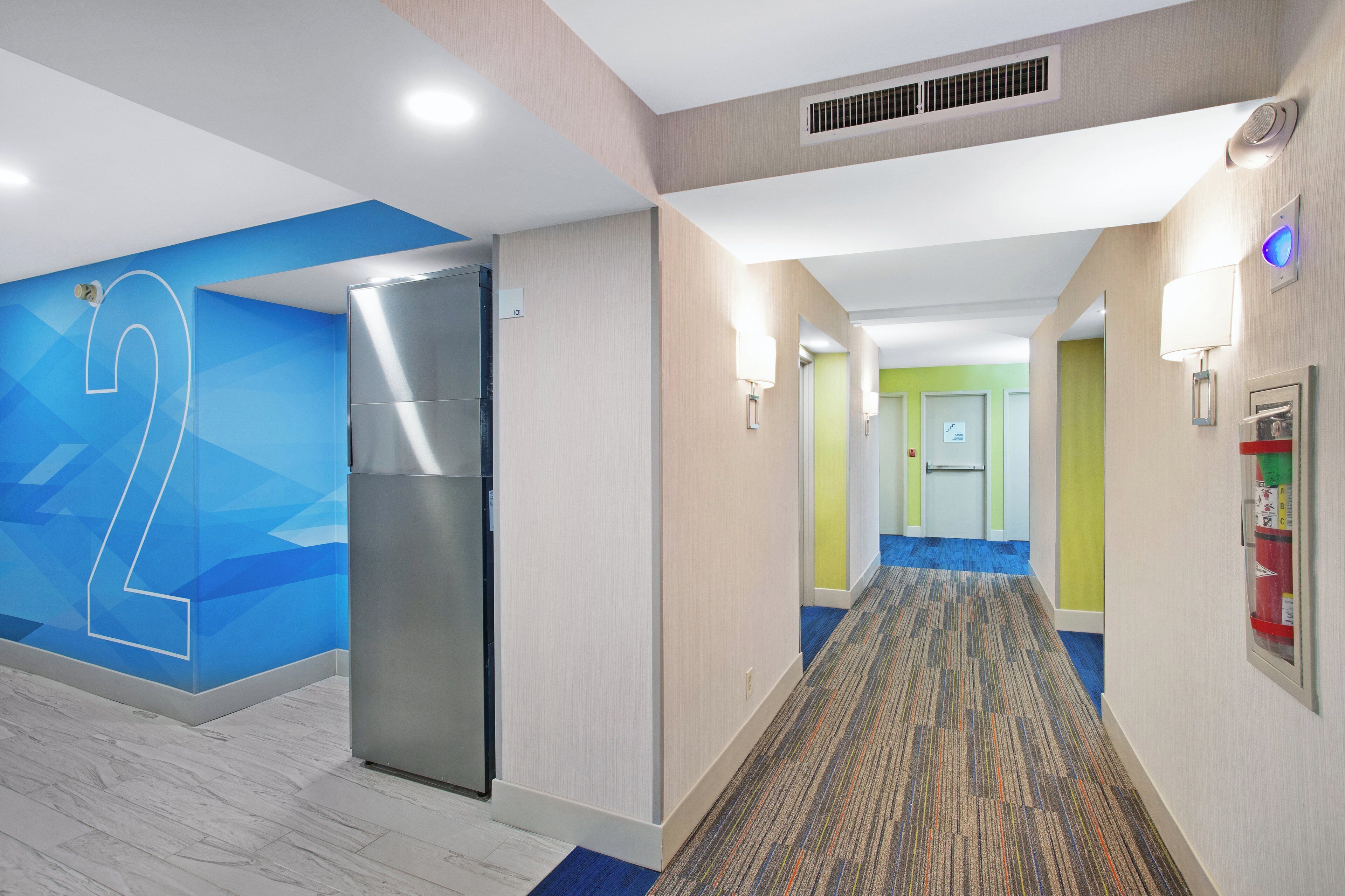 A hotel corridor with a modern design, including a large number '2' on the wall, a refrigerator, and a fire extinguisher.