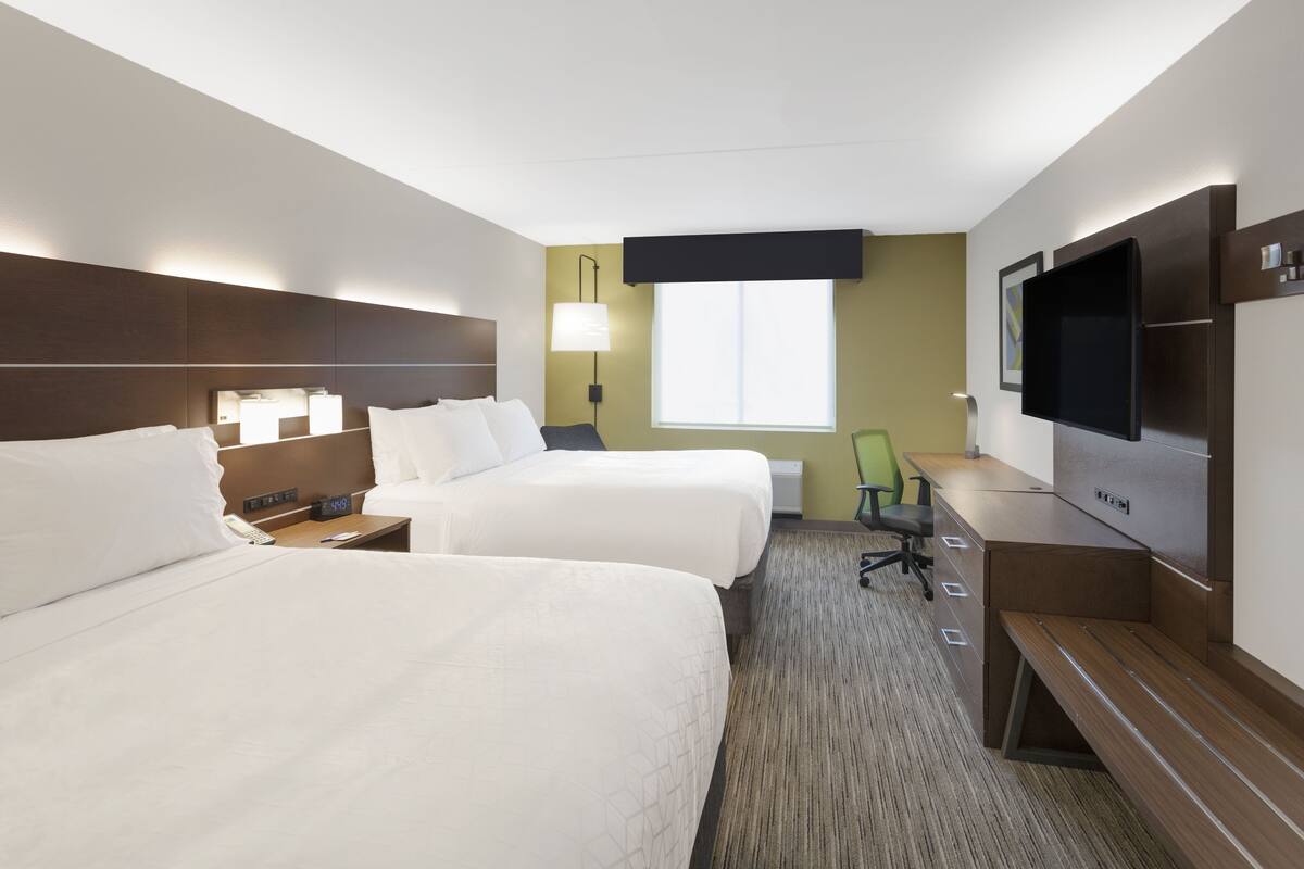 A hotel room with two beds, a desk, a chair, a TV, and a window.