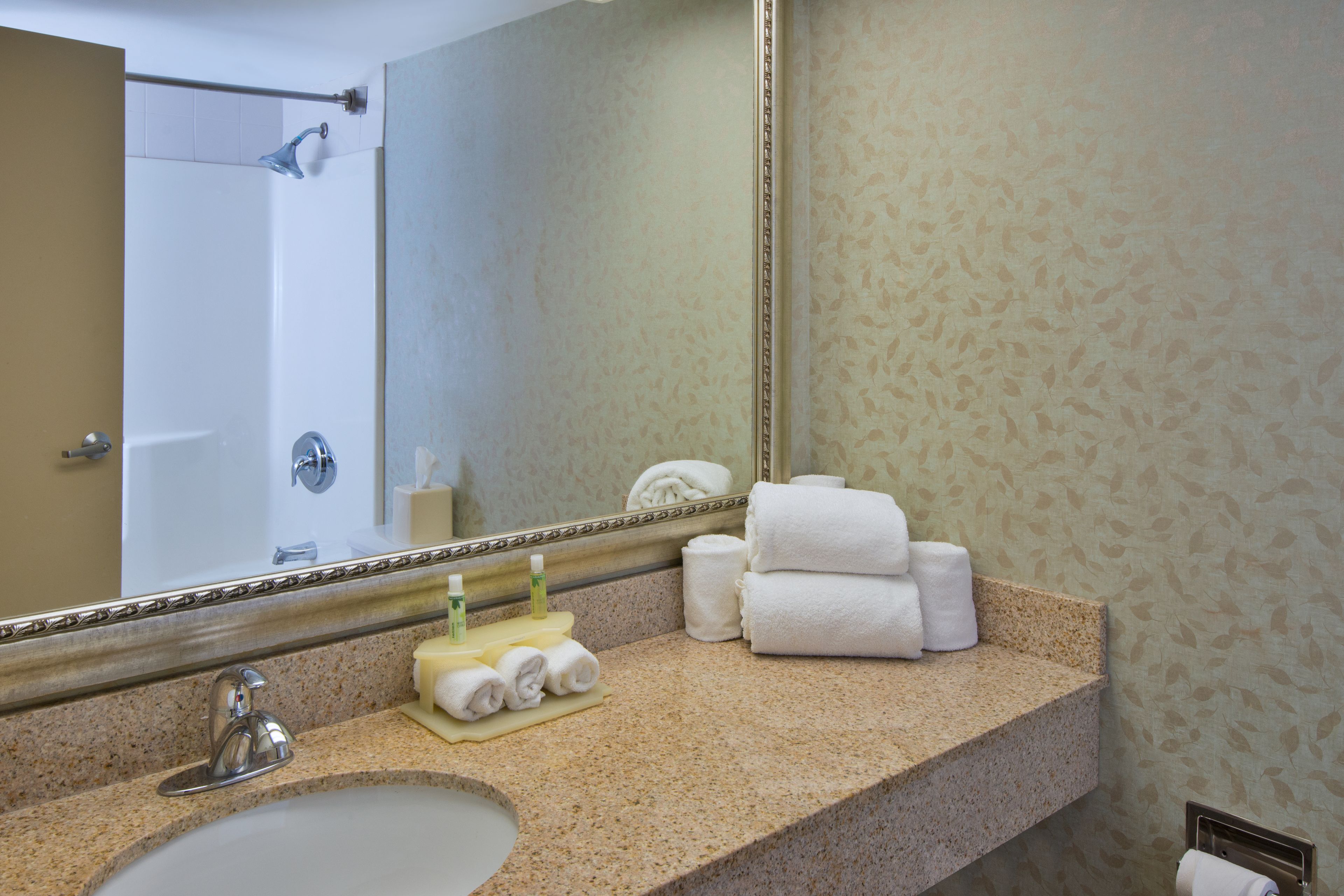 A bathroom with a sink, mirror, towels, and toiletries.