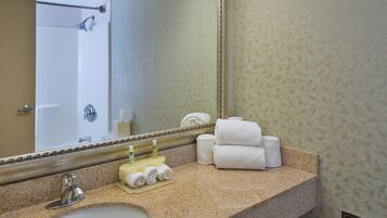 A bathroom with a sink, mirror, towels, and toiletries.