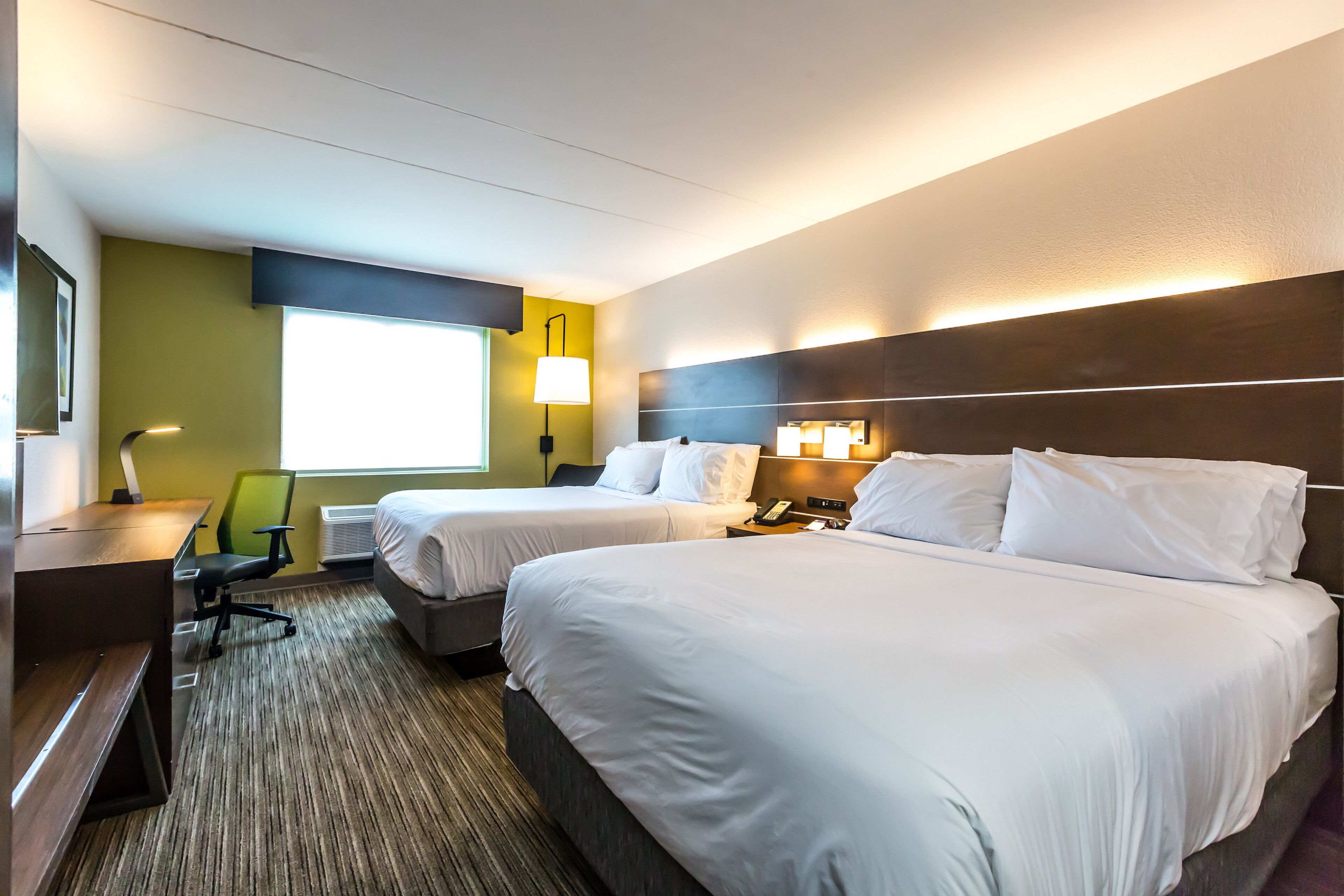 Une chambre d’hôtel avec deux lits, un bureau, une chaise et une fenêtre.