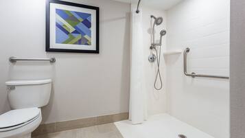 Un baño con inodoro, ducha con barras de apoyo y una obra de arte abstracto enmarcada en la pared.