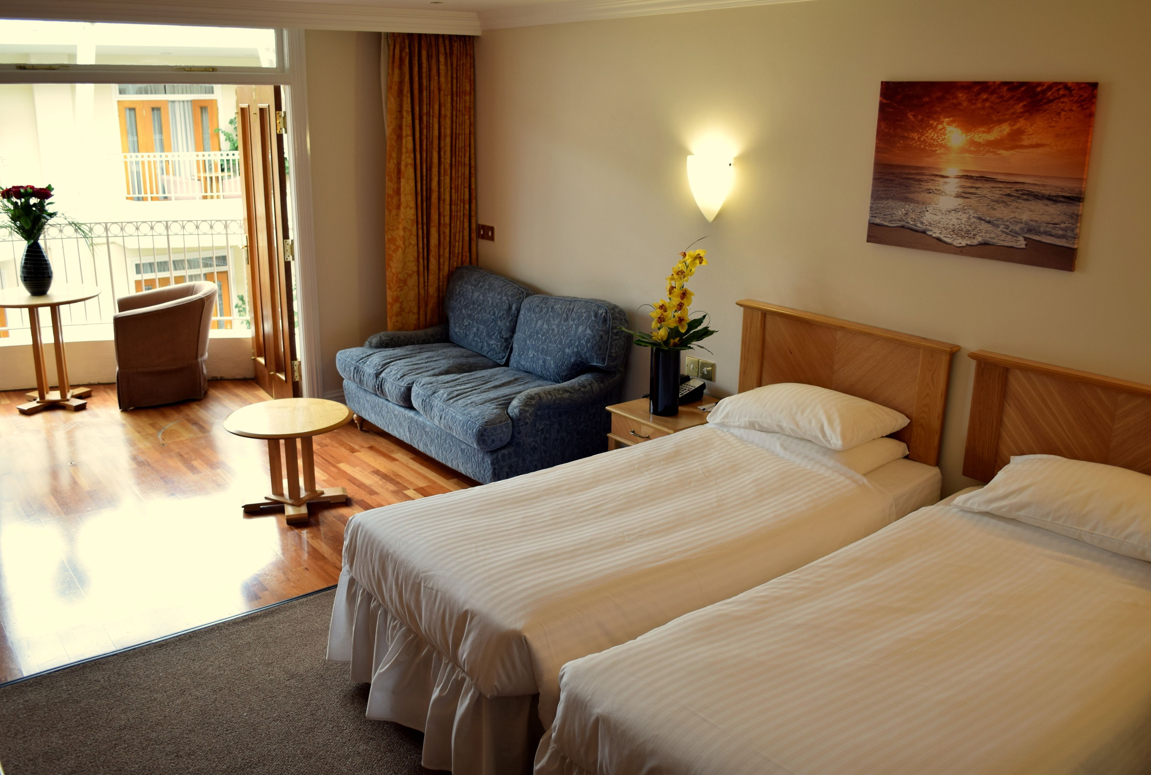 Ett hotellrum med två sängar, en soffa, ett litet bord och utsikt över balkongen.