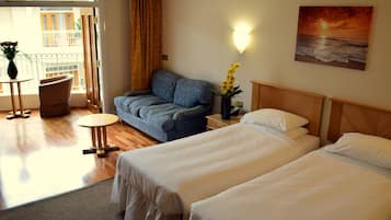 A hotel room with two beds, a sofa, a small table, and a view of the outside balcony.