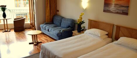 Ett hotellrum med två sängar, en soffa, ett litet bord och utsikt över balkongen.