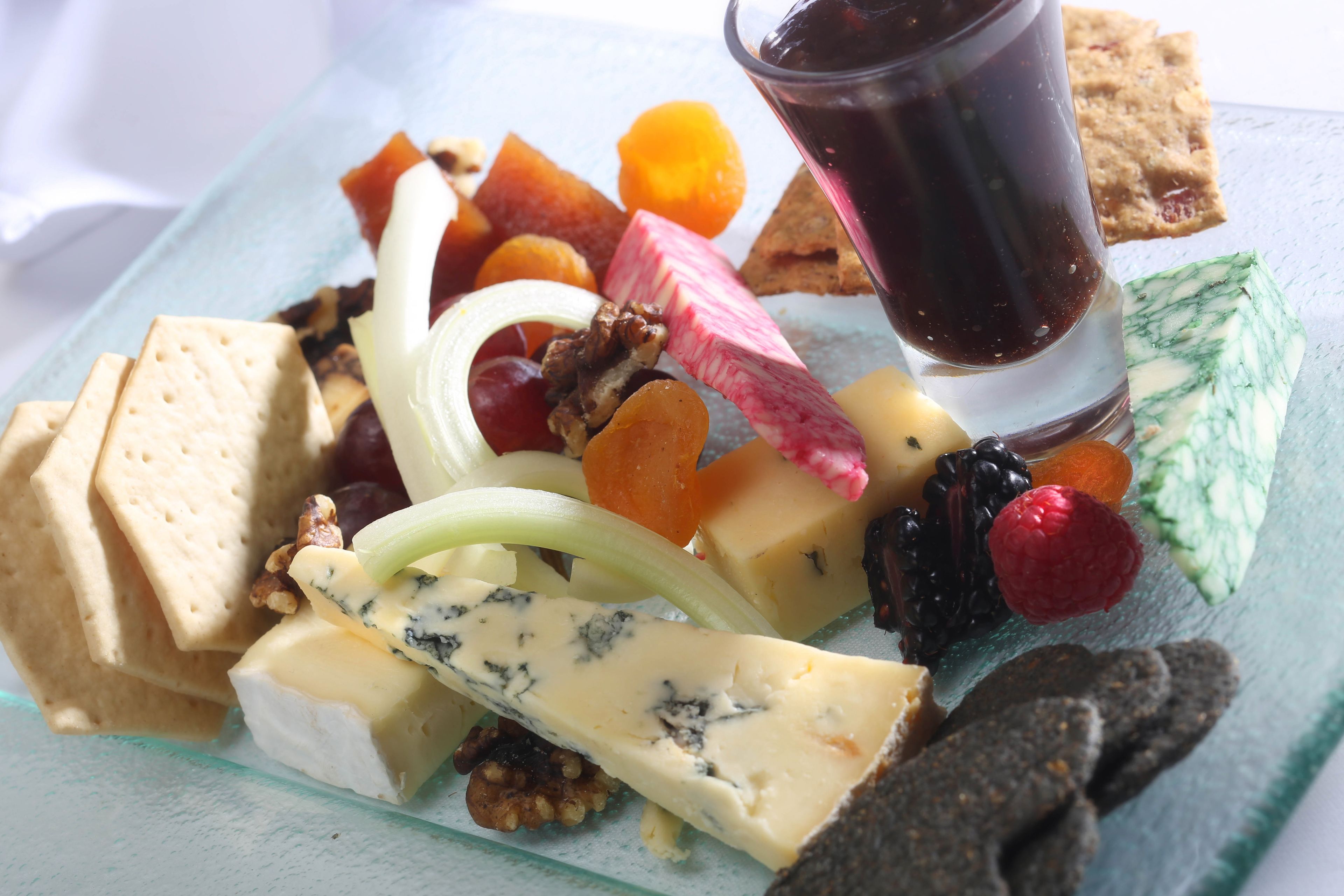 A variety of cheeses, fruits, nuts, and crackers on a glass plate.