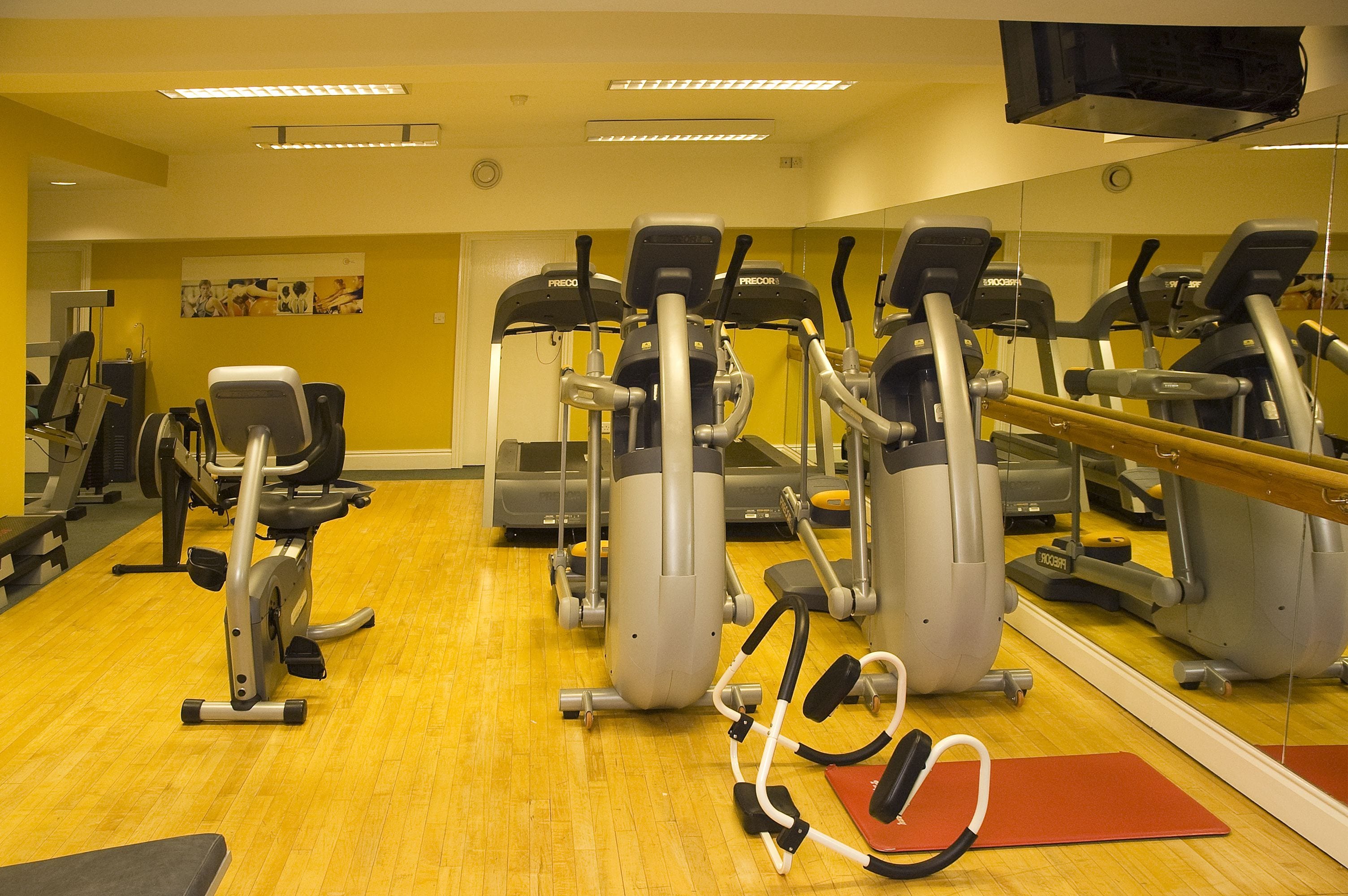 A gym with exercise equipment, mirrors, and a wooden floor.
