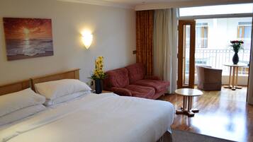 Habitación de hotel con cama, sofá, una mesita y balcón con vistas.