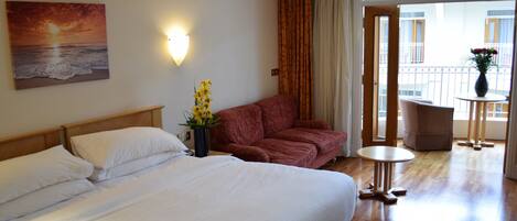 Habitación de hotel con cama, sofá, una mesita y balcón con vistas.