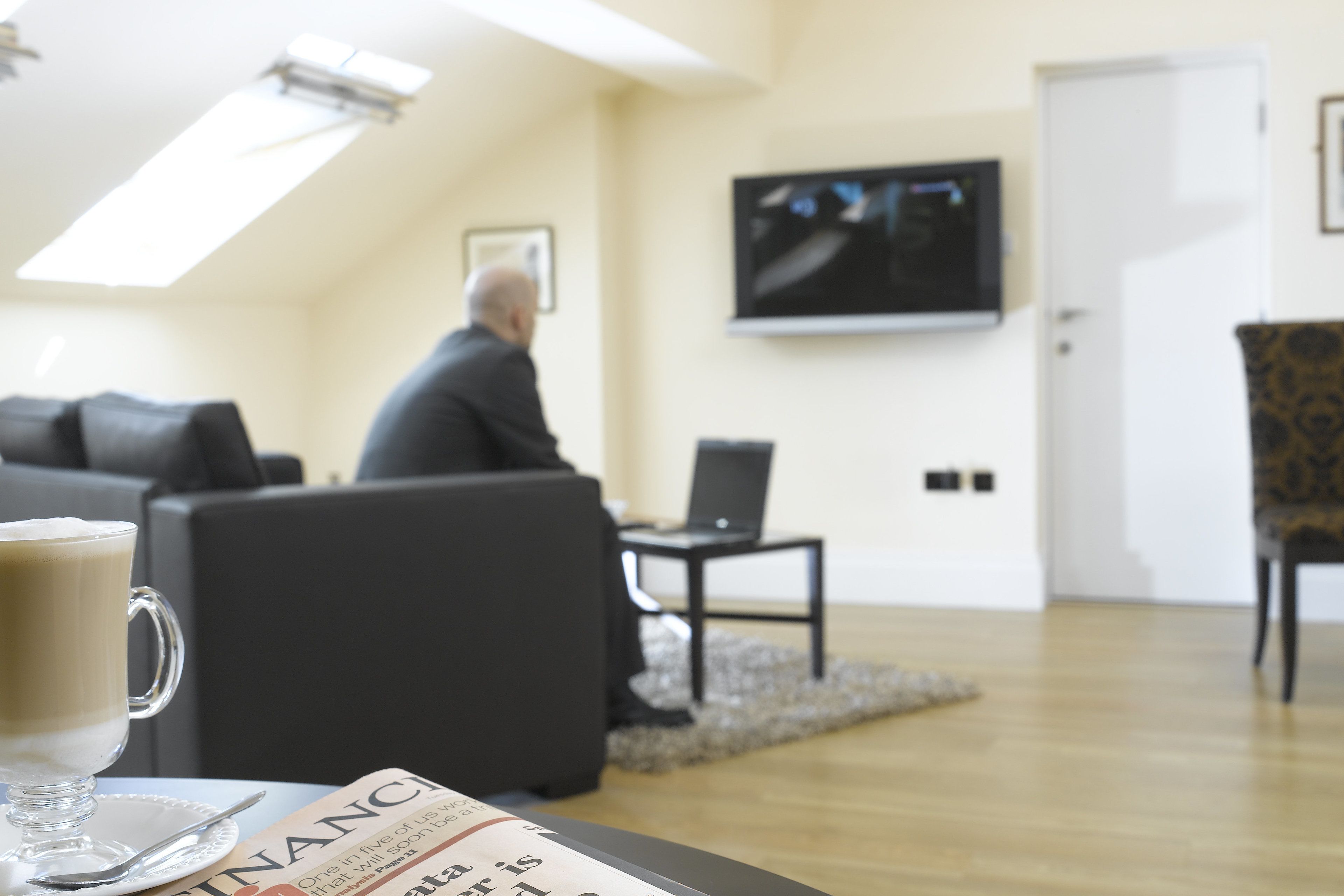 A living room with a sofa, a coffee table with a newspaper, and a television on the wall.