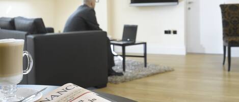 A living room with a sofa, a coffee table with a newspaper, and a television on the wall.