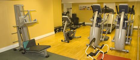 Een fitnessruimte met diverse trainingsapparaten, een bank en een mat.