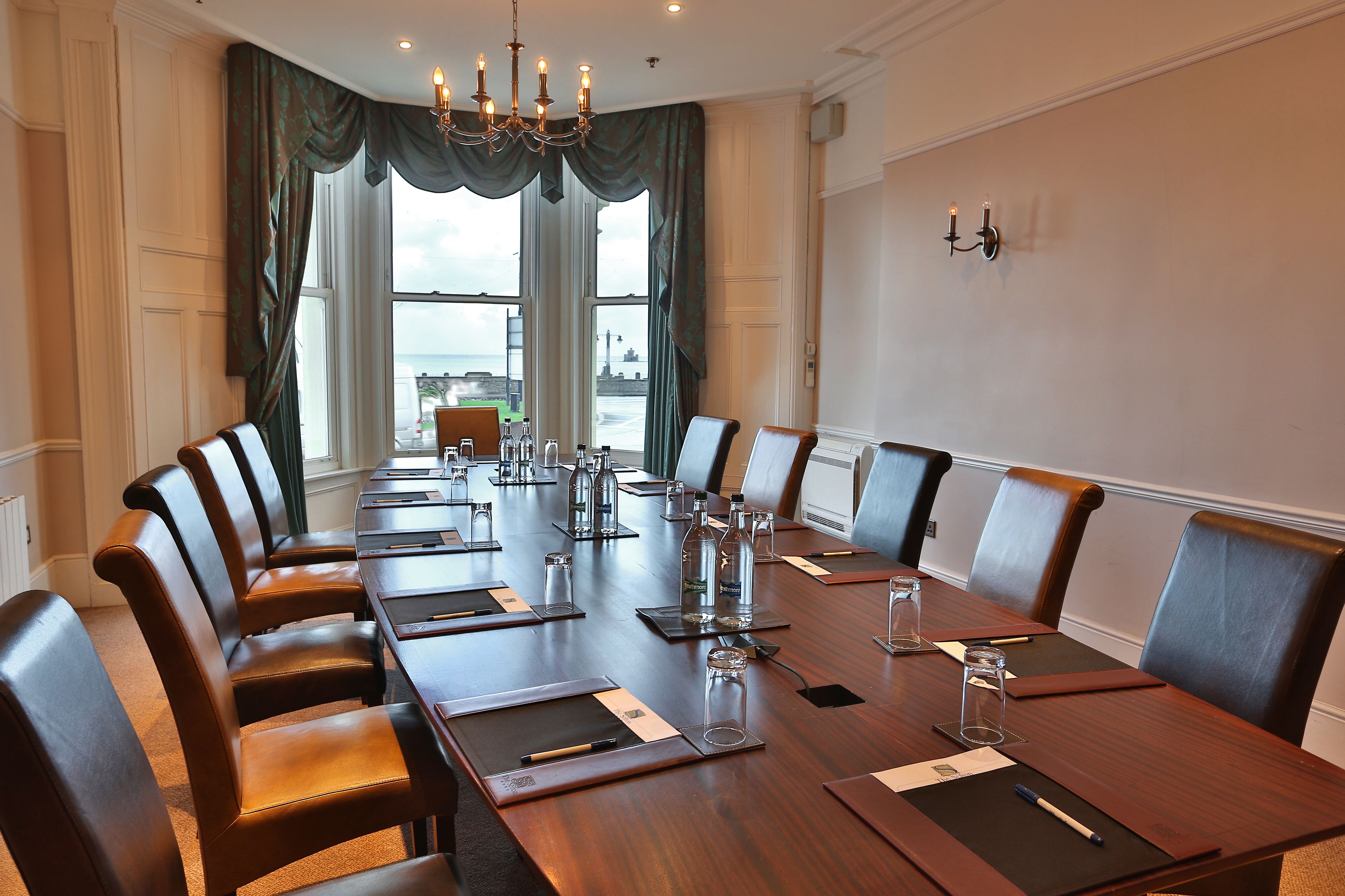 Une salle de conférence dotée d’une longue table en bois, de fauteuils en cuir et offrant une vue sur la mer grâce à de grandes fenêtres.