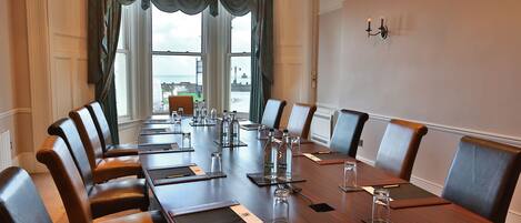 Un salón de conferencias con una larga mesa de madera, sillas de cuero y vistas al mar a través de amplios ventanales.