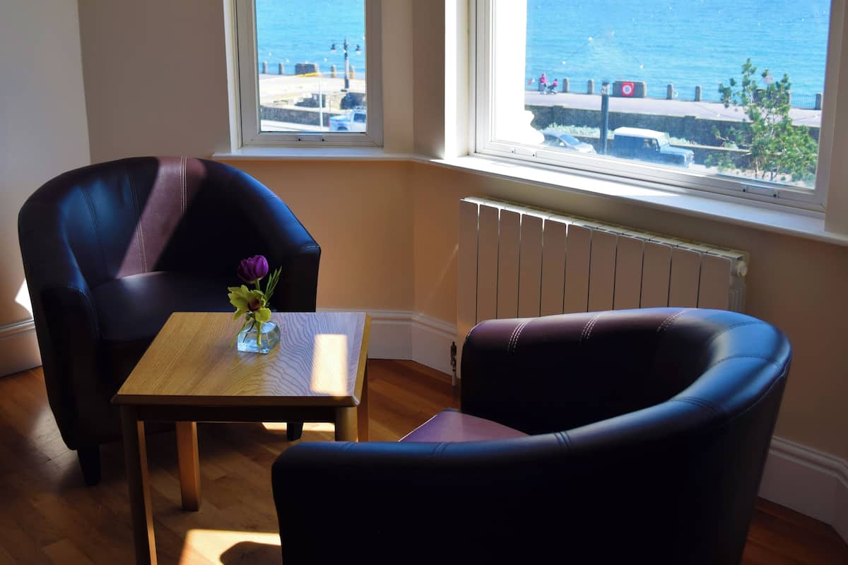 A room with a view of the sea, a table with a vase, and two chairs.