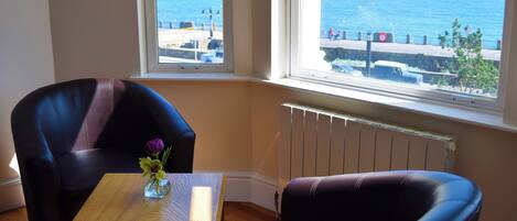 Una habitación con vista al mar, una mesa con un florero y dos sillas.