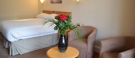 A hotel room with a bed, a round wooden table with a vase of flowers, and two armchairs.