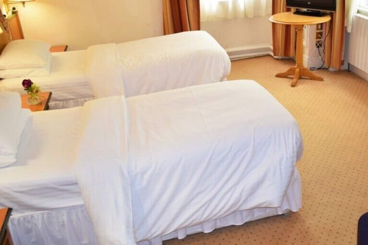 A hotel room with two single beds, a small table, a television, and a window with curtains.