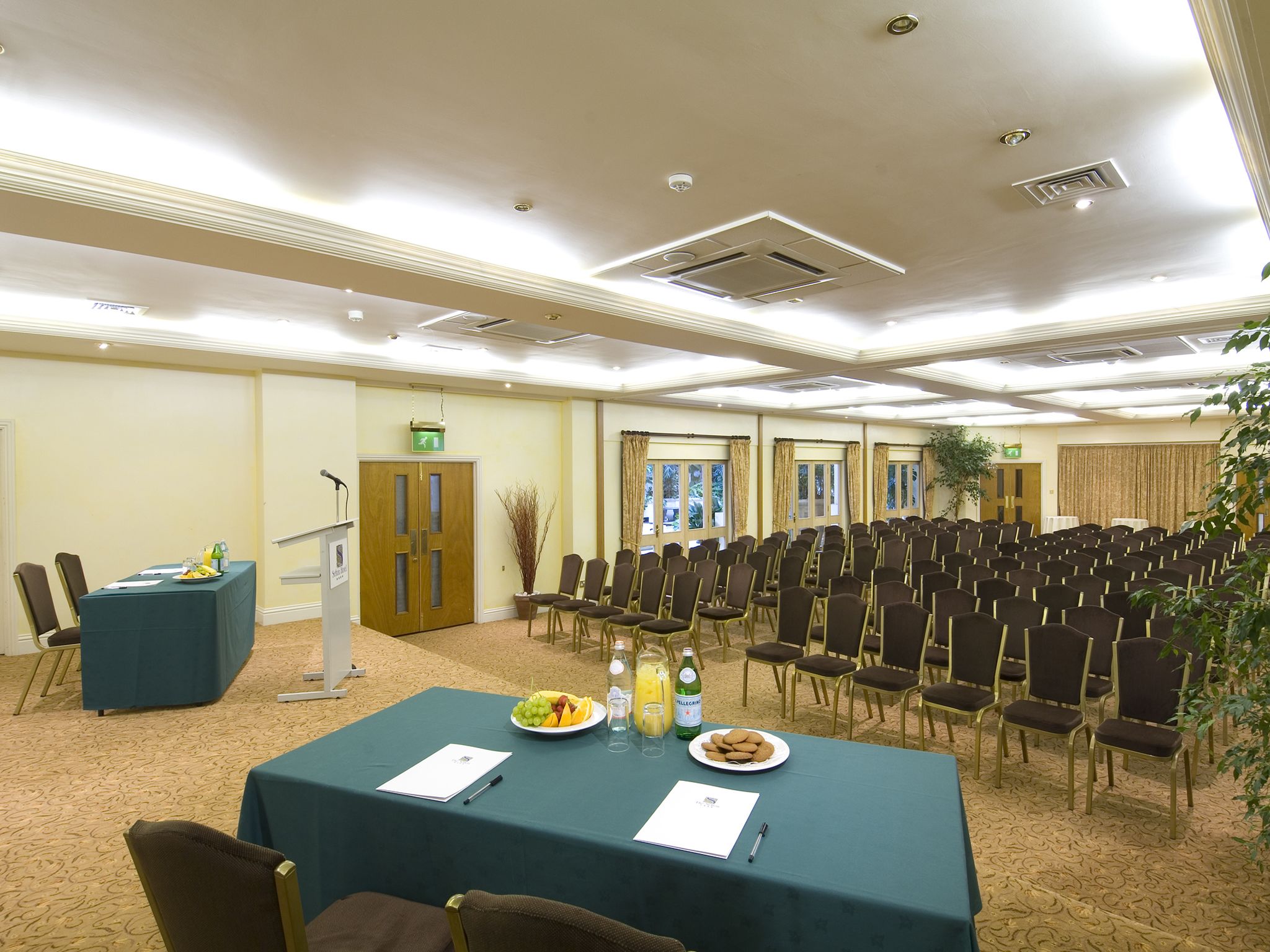 Un salón de conferencias con filas de sillas, un atril y mesas con comida y bebidas.