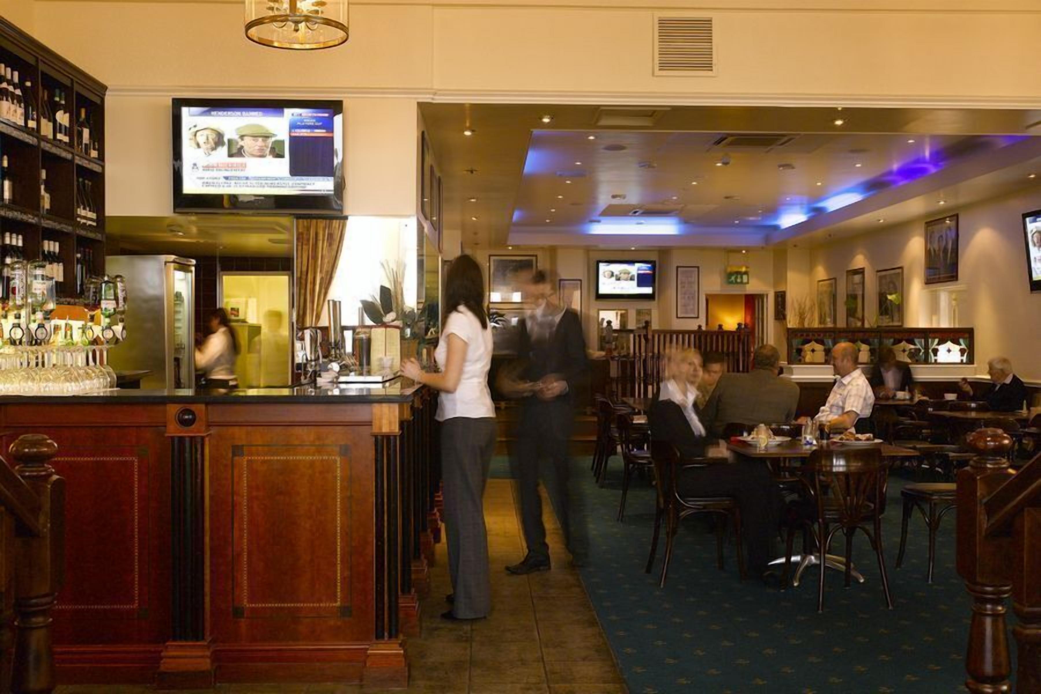 A bar area with a counter, multiple televisions, and a seating area with tables and chairs.