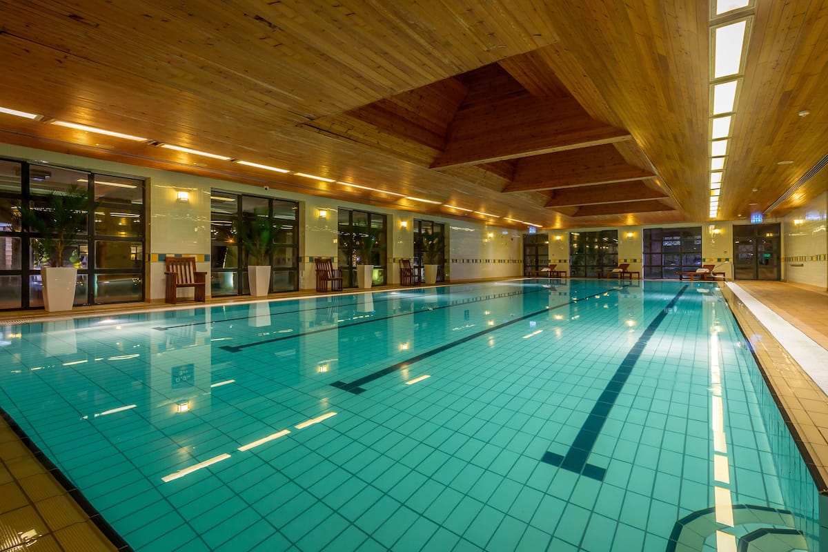 Une piscine intérieure dotée de lignes de démarcation bien visibles, de poutres en bois au plafond et de grandes fenêtres laissant entrer la lumière naturelle.