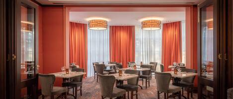 Un comedor con mesas y sillas, cortinas rojas y lámparas colgantes.