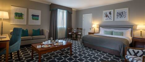 A hotel room with a bed, a sofa, a coffee table, and artwork on the walls.