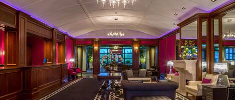A spacious lobby with a high ceiling, chandeliers, and a central seating area with sofas and a coffee table.