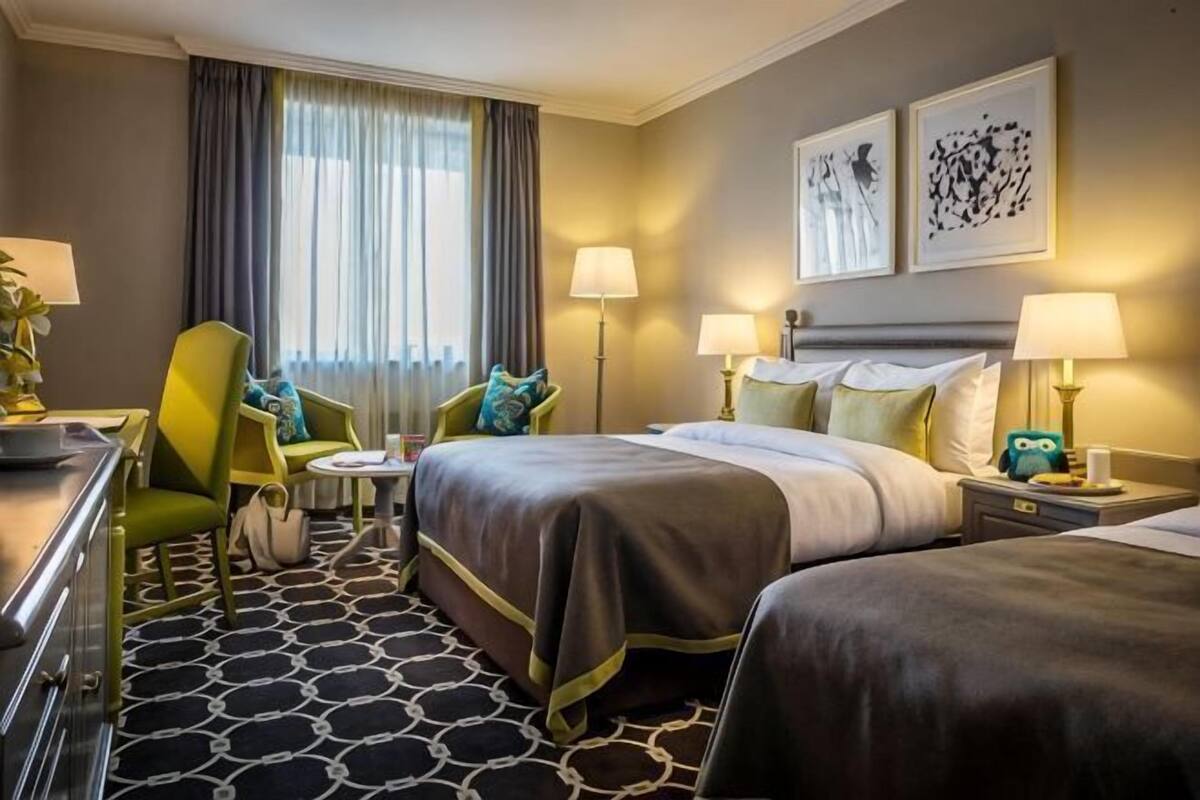 Une chambre d’hôtel avec deux lits, un bureau, une chaise, une petite table et une fenêtre avec des rideaux.