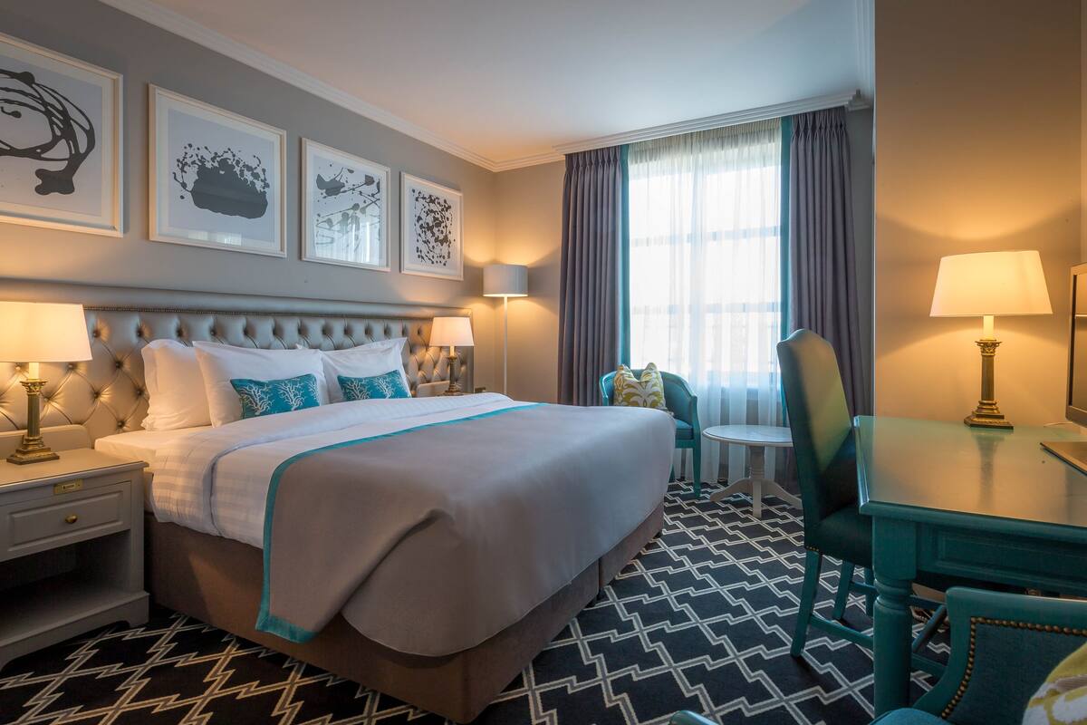 Une chambre d’hôtel avec un grand lit, deux tables de chevet avec des lampes, un bureau avec une chaise et une fenêtre avec des rideaux.
