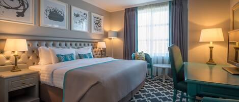 Habitación de hotel con una cama grande, dos mesitas de noche con lámparas, un escritorio con silla y una ventana con cortinas.