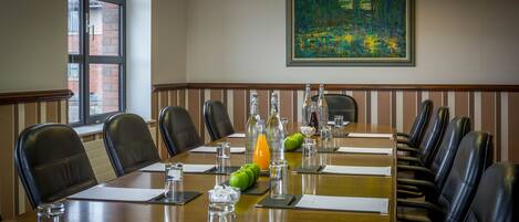 A conference room with a long table, leather chairs, water bottles, and a painting on the wall.