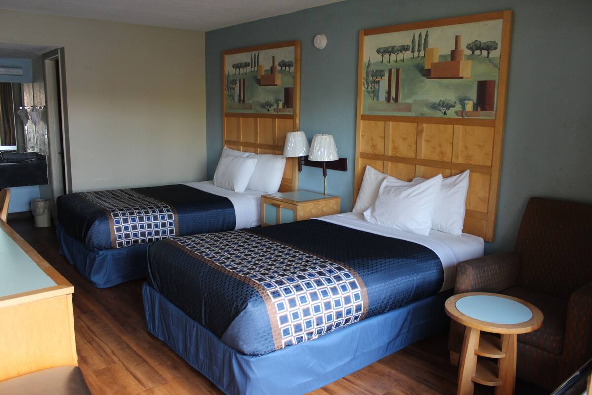 Ein Hotelzimmer mit zwei Betten, einem kleinen Tisch, einem Stuhl und zwei Bildern an der Wand.
