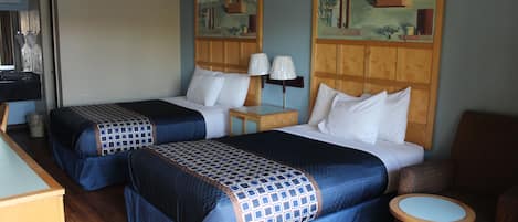 A hotel room with two beds, a small table, a chair, and two paintings on the wall.
