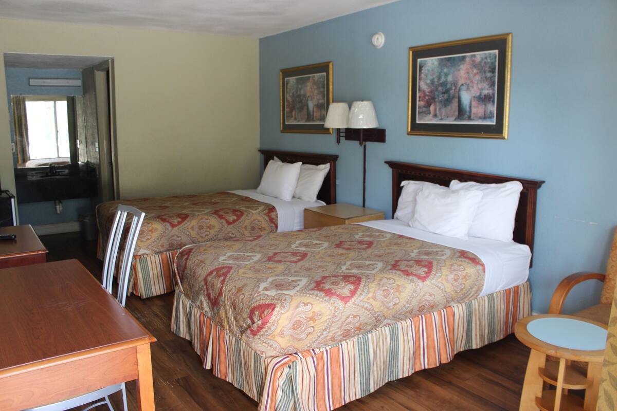 Ein Hotelzimmer mit zwei Betten, einem Schreibtisch, einem Sessel und zwei Bildern an der Wand.