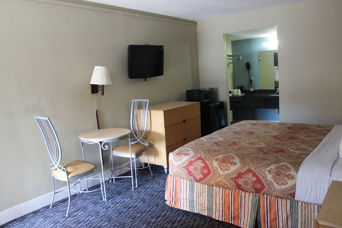 Ein Hotelzimmer mit einem Bett, einem Schreibtisch mit Stuhl, einem Fernseher, einer Mikrowelle und einem Schminktisch.