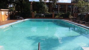 Ein klares Schwimmbecken mit Metallleiter, umgeben von einem Zaun und Gartenmöbeln.