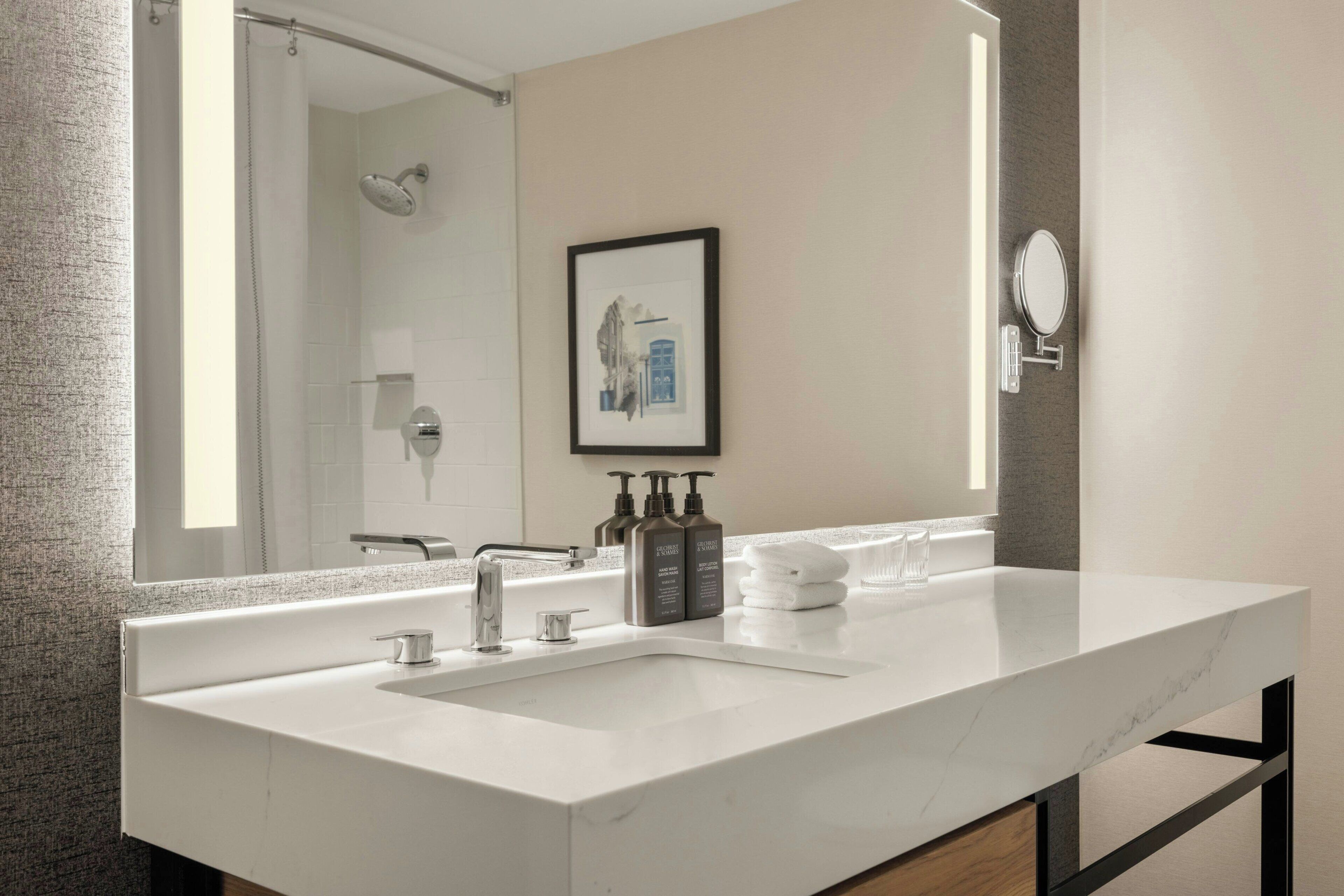 Une salle de bain moderne avec un lavabo en marbre blanc, un grand miroir et un tableau encadré au mur.