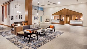 A spacious lobby with a modern design, featuring a seating area with sofas and chairs, a coffee table, and a reception desk with a wooden accent wall.