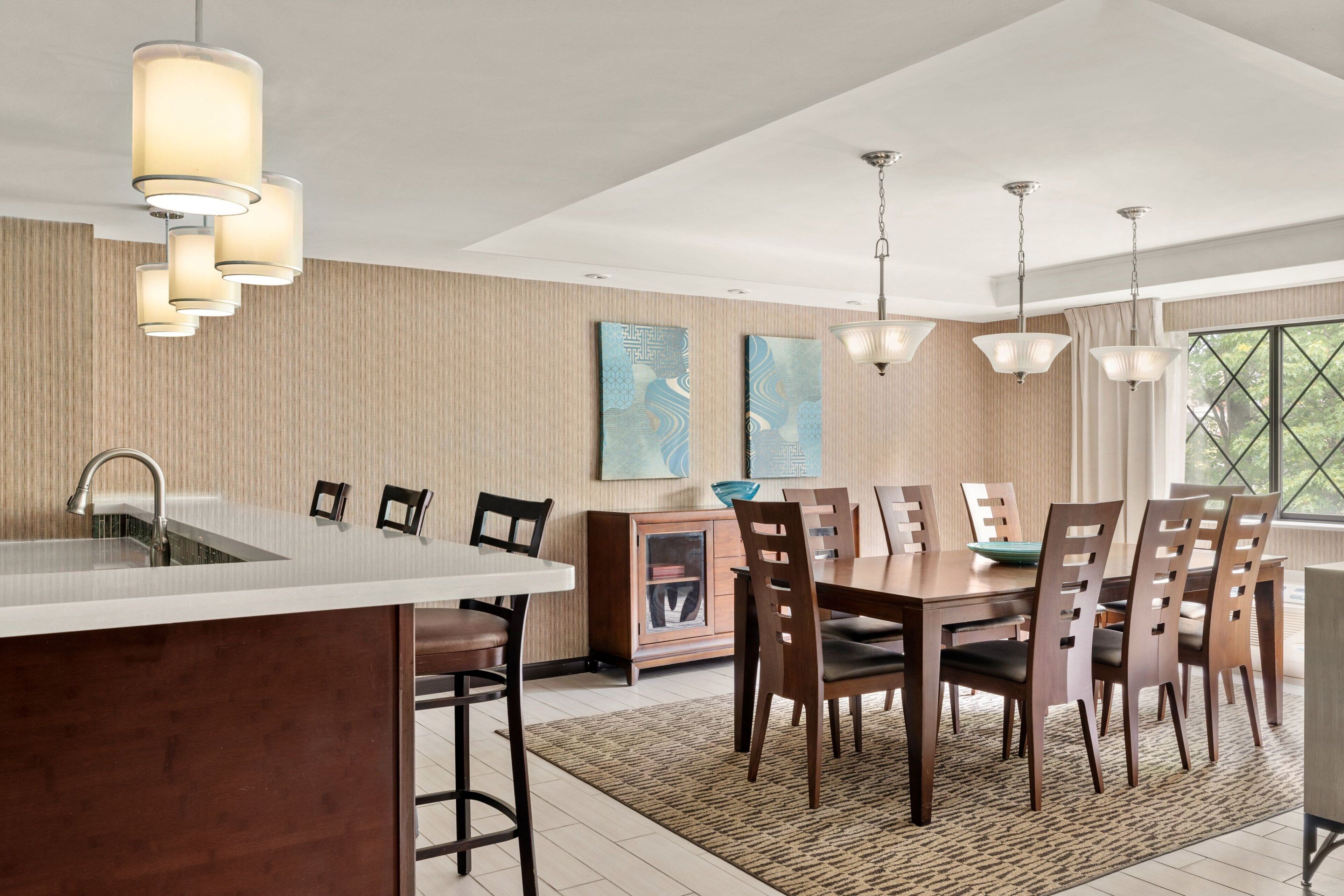 A modern kitchen with a central island, wooden dining table, and pendant lighting.
