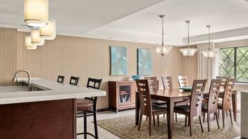 A modern kitchen with a central island, wooden dining table, and pendant lighting.