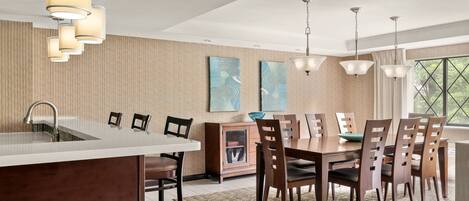 A modern kitchen with a central island, wooden dining table, and pendant lighting.