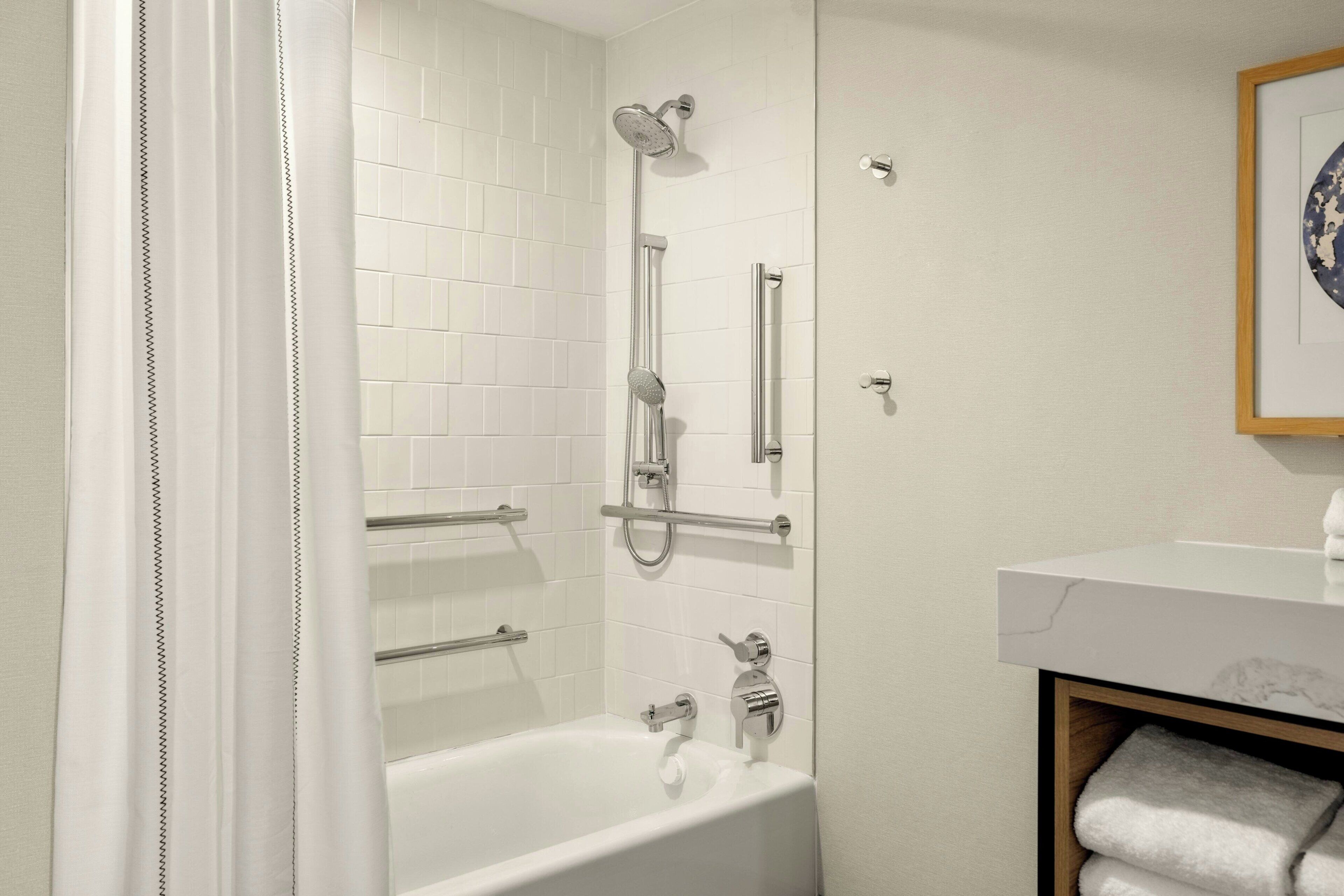 A modern bathroom with a white bathtub, a shower with a handheld showerhead, and a towel rack.