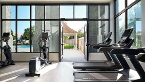 Un gimnasio con cintas de correr y elípticas, ventanas amplias y vistas a una piscina y zona exterior.