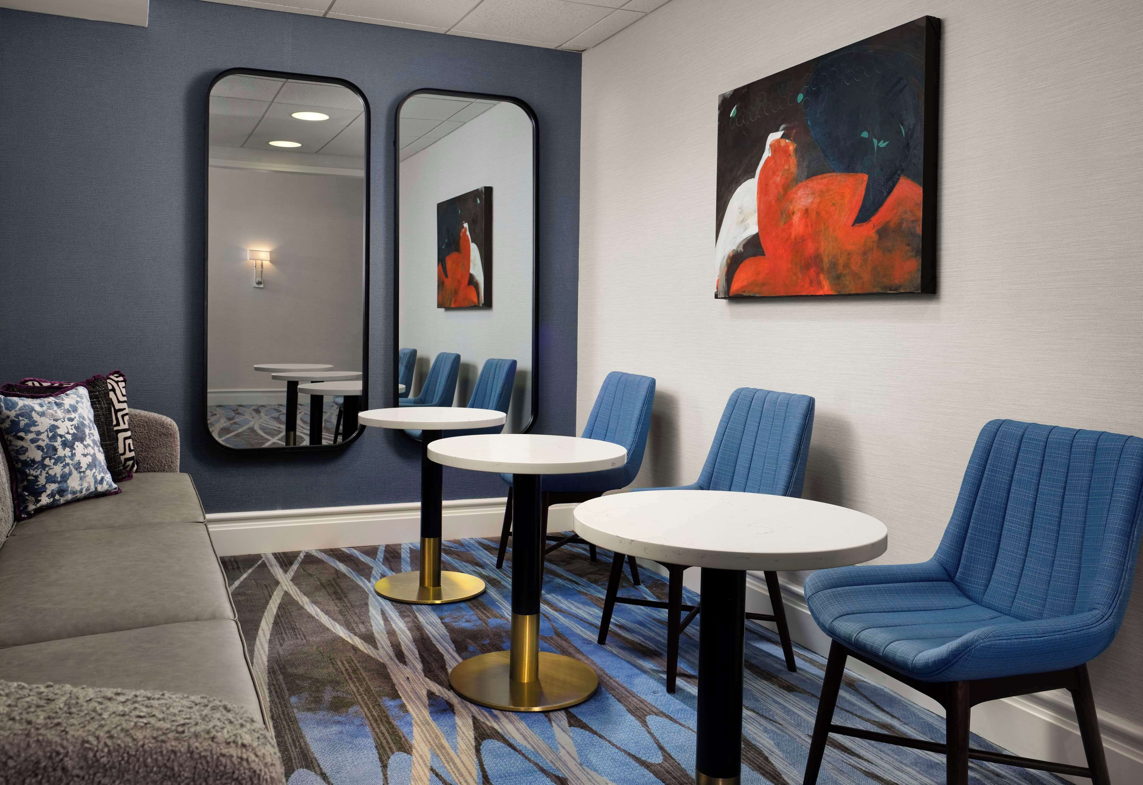 A hotel lobby with a sofa, two round tables, blue chairs, a large mirror, and a painting on the wall.