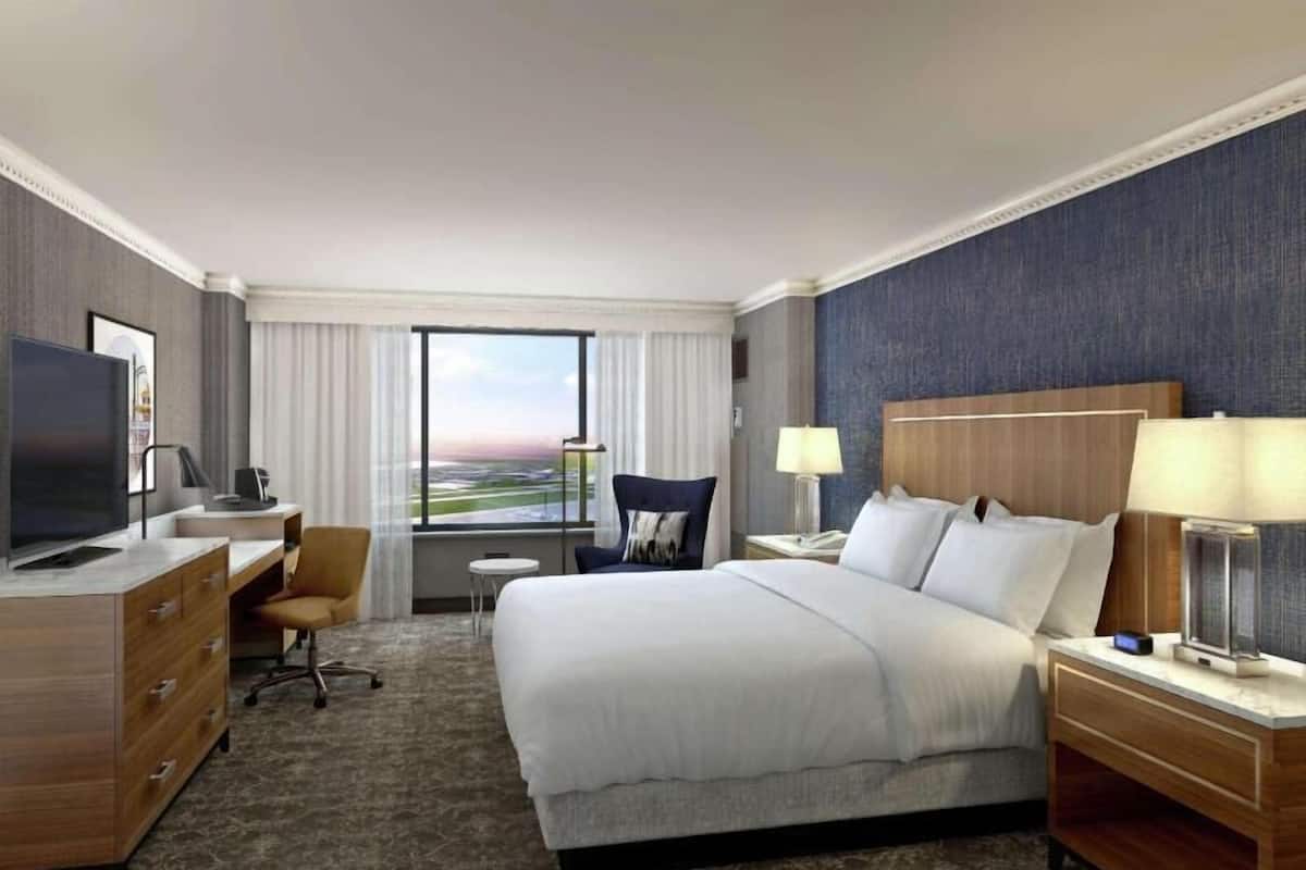 Een hotelkamer met een groot bed, een bureau met een televisie, een stoel, een klein tafeltje en uitzicht op het landschap.